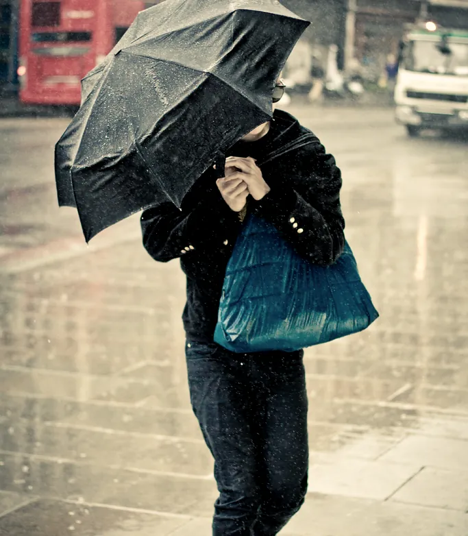 A figure sheltering under an umbrella in heavy rain